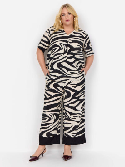 model zebra t-shirt og hænderne i lommerne på bukser med zebraprint og brede sorte kante spå buksebenene. Wasabi WA-LUANA 3 Bukser Black Combi